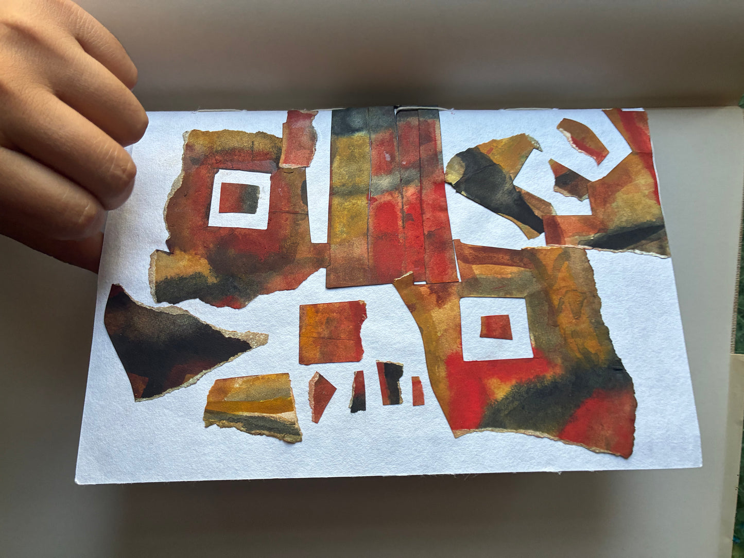 Abstract art piece with geometric shapes on a white background, held by a hand.